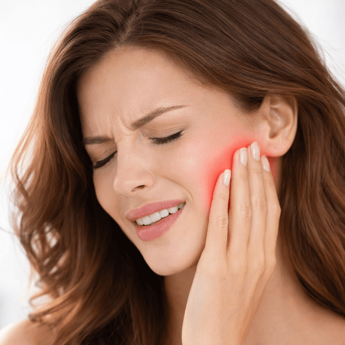 Frau berührt schmerzhaft die Kaumuskulatur bei Kaumuskelverspannung in einer ästhetisch-medizinischen Behandlungssituation